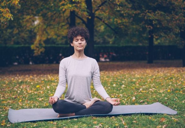Good-looking girl in sports clothing is twisting her body sitting in lotus position then relaxing with closed eyes after practice in town park on autumn day.