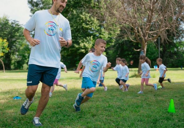 A group of kids running with an instructor during outdoor sports activities on a sunny day in a park.