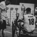 An athlete using a rowing machine indoors, coached in a gym setting.