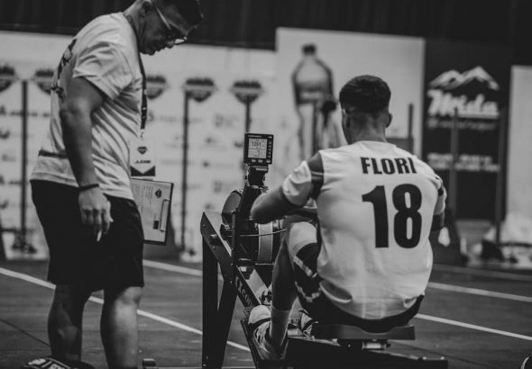 An athlete using a rowing machine indoors, coached in a gym setting.